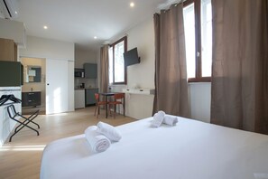 A hotel room with a bed, towels, a desk, a chair, and a TV mounted on the wall. - Gab House (Bron)