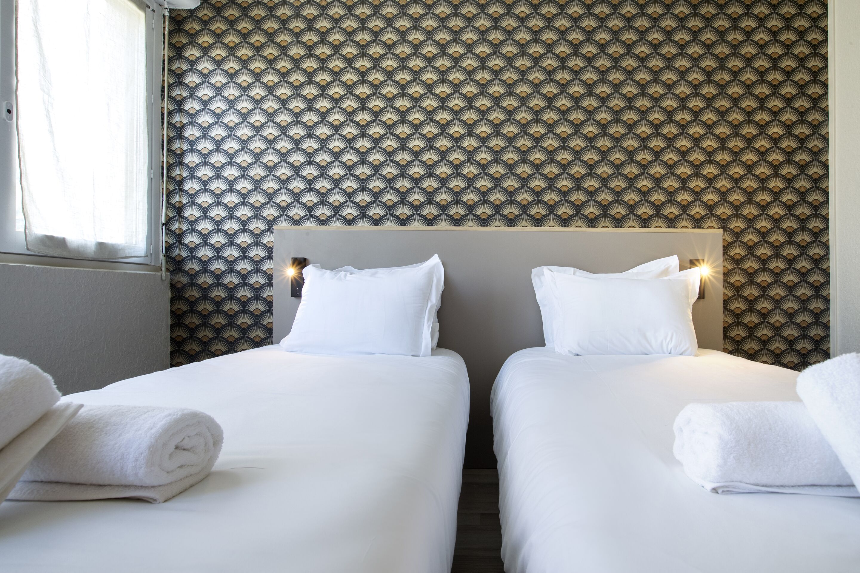 Ein Hotelzimmer mit zwei Betten, weißen Laken und einer gemusterten Tapete.