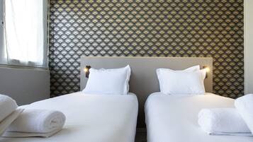 Ein Hotelzimmer mit zwei Betten, weißen Laken und einer gemusterten Tapete.