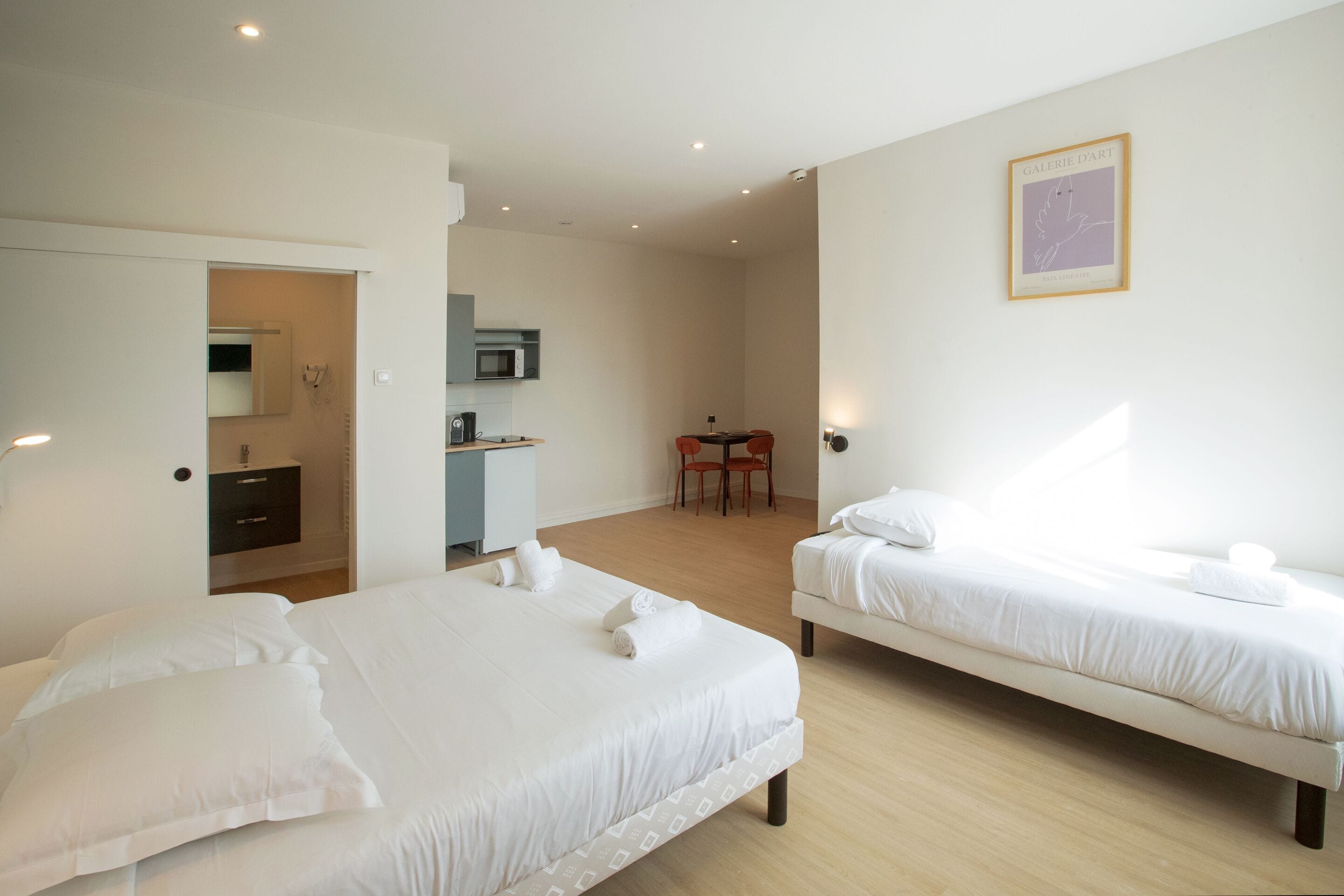 A hotel room with two beds, a desk, a chair, a microwave, and a framed artwork on the wall.