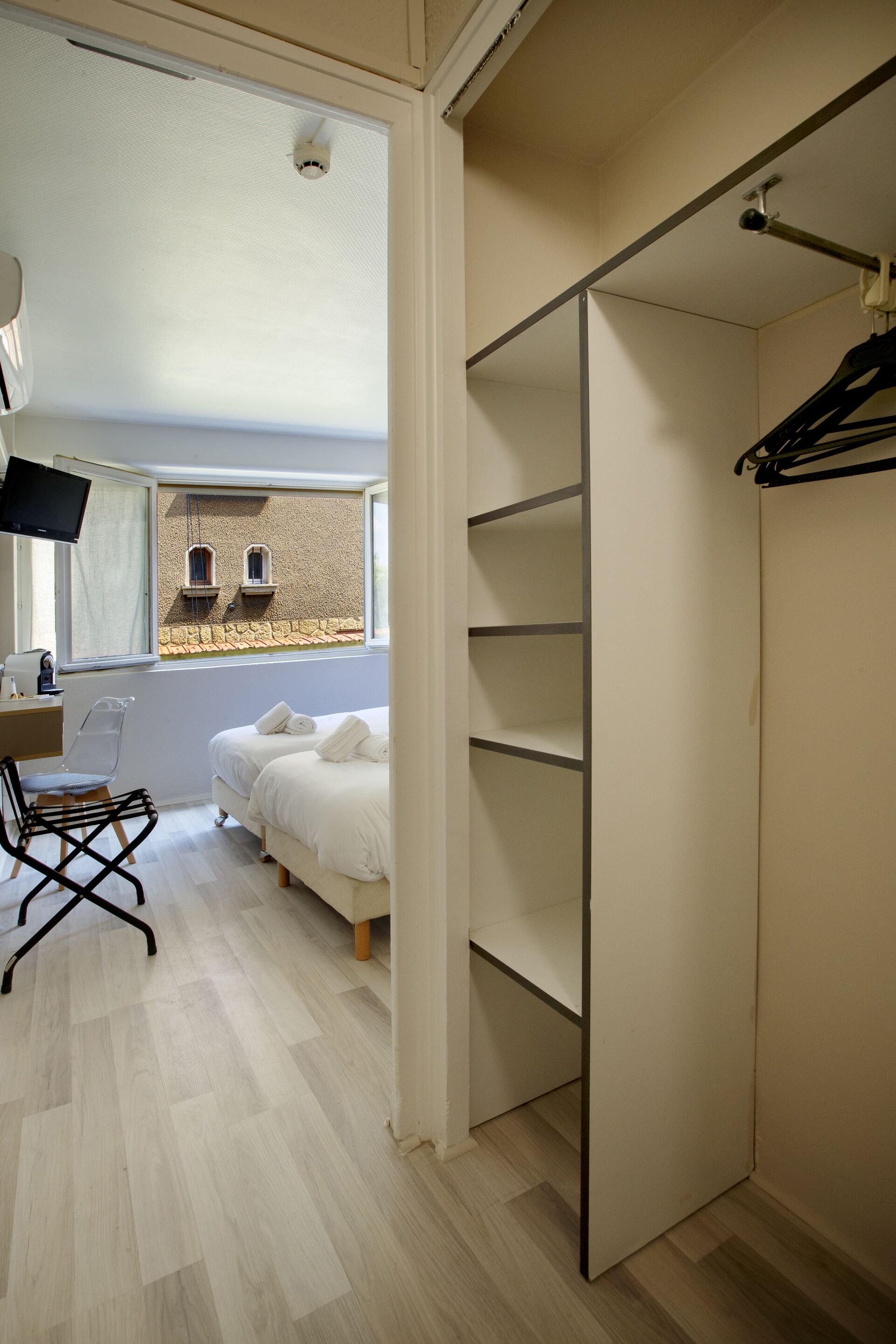 Une chambre à coucher comprenant un lit, un bureau avec une chaise, un téléviseur et une fenêtre donnant sur un immeuble.