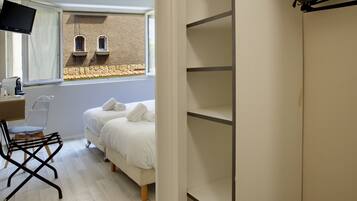 Une chambre à coucher comprenant un lit, un bureau avec une chaise, un téléviseur et une fenêtre donnant sur un immeuble.