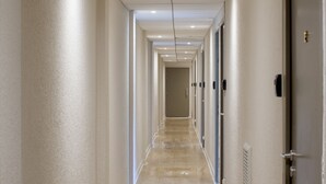 Passadís llarg i estret amb un terra polit, parets blanques i portes a un costat.