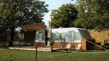 Una caravana con porche cubierto, un pequeño jardín y una terraza de madera.