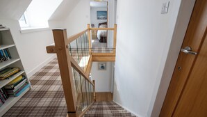 A staircase with wooden railings and a checkered carpet leading to a bedroom with a bed and a painting on the wall. - A charming cottage in the heart of Ballater, with a beautiful & modern interior (Ballater)