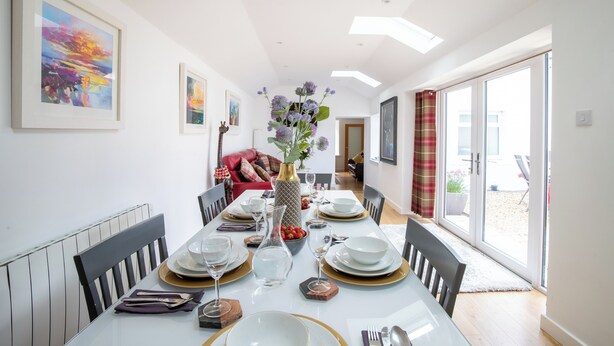 A dining area with a long table set for four, flanked by chairs, with a vase of flowers in the center. - A charming cottage in the heart of Ballater, with a beautiful & modern interior (Ballater)