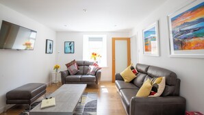 A modern living room with two sofas, a coffee table, and a flat-screen TV. - A charming cottage in the heart of Ballater, with a beautiful & modern interior (Ballater)