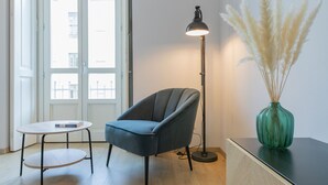 Una habitación moderna con un sillón gris, una pequeña mesa redonda, una lámpara de pie y un jarrón verde con plumas de paniculata.