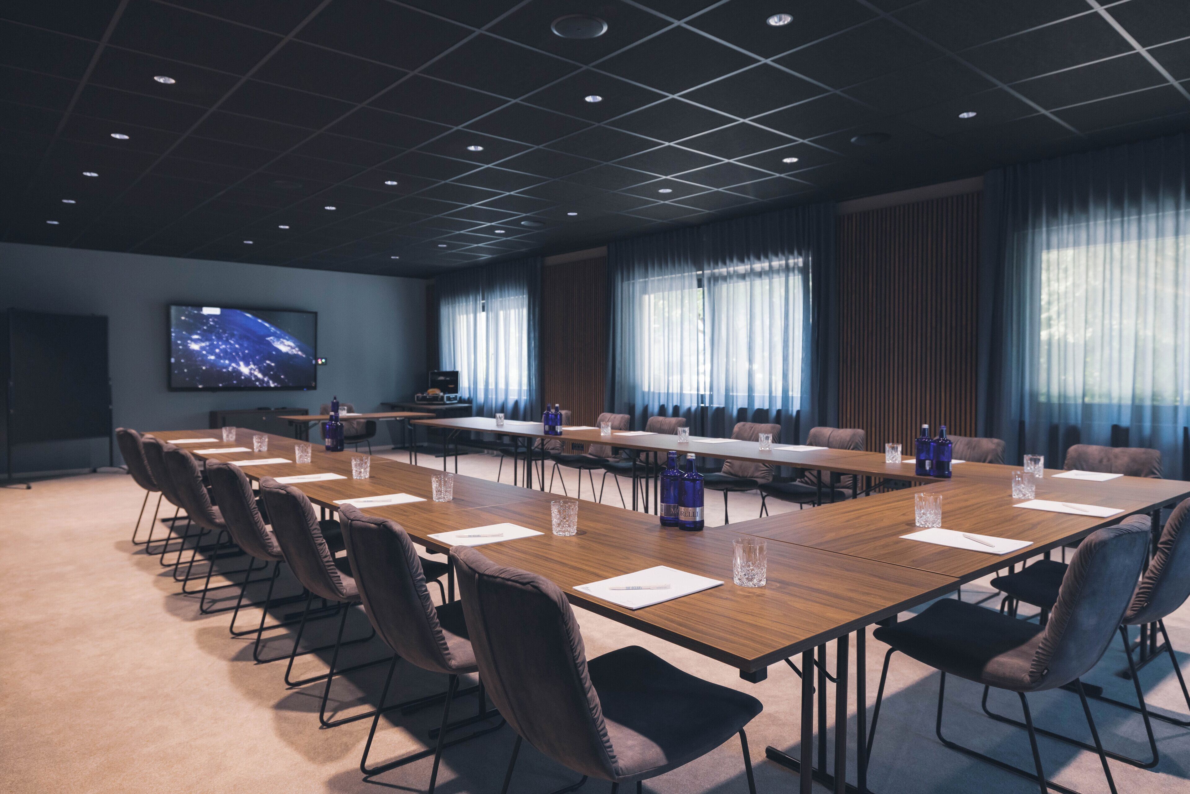 Un salón de conferencias con una larga mesa, sillas y una pantalla de televisión mostrando un paisaje urbano.