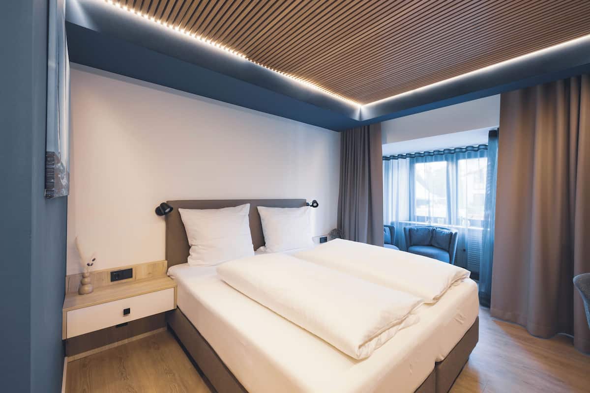 A modern hotel room with a large bed, a bedside table, a nightstand, and a window with curtains.