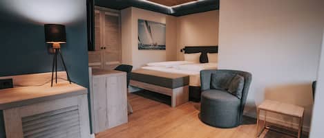 A modern bedroom with a bed, bedside table, chair, and a desk with a lamp.