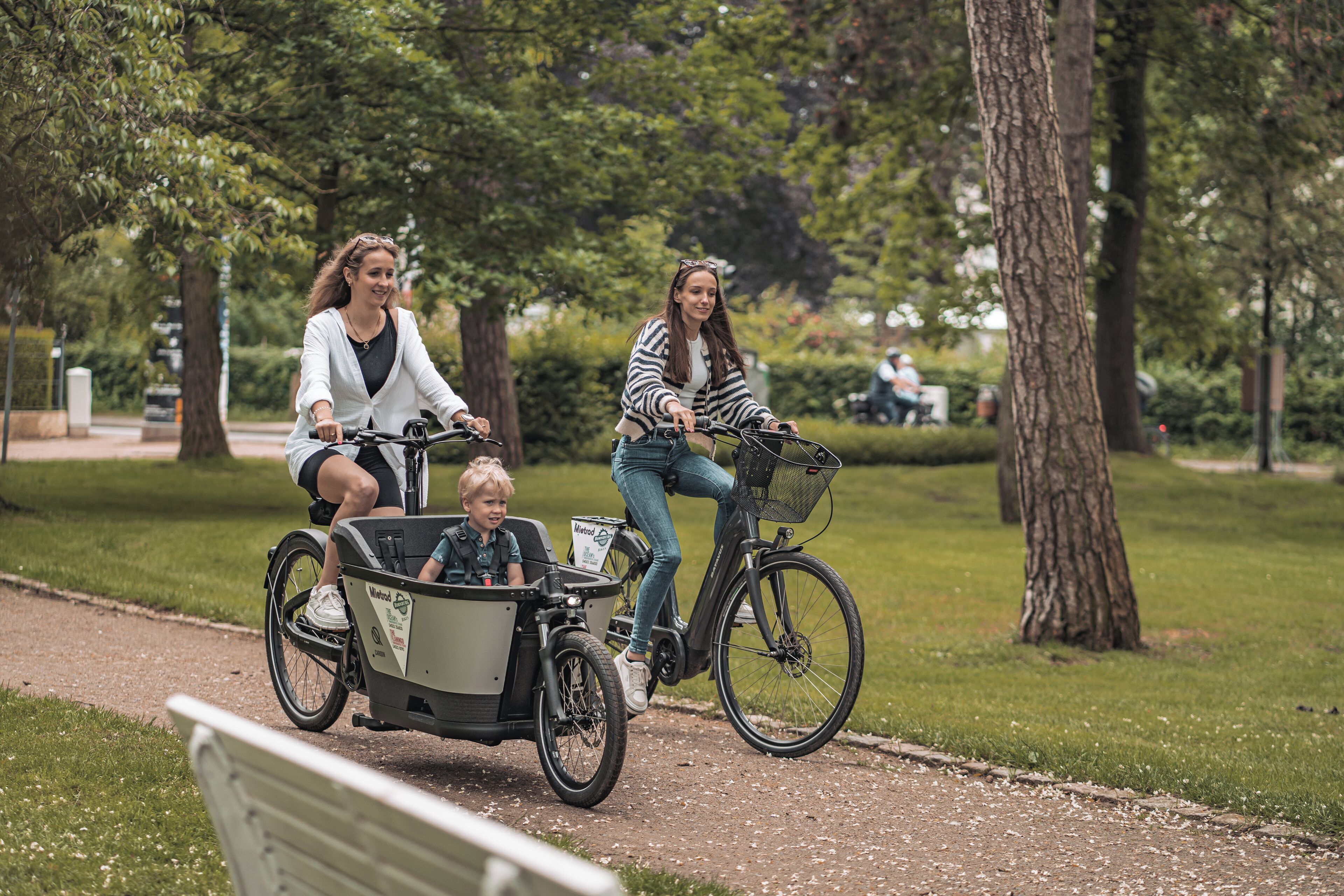 Um caminho no parque com duas bicicletas, uma delas com um reboque, e um banco em primeiro plano.