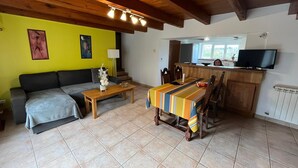 A living room with a sofa, a coffee table, a dining table with chairs, a TV, and a kitchen area with a window. - Country house with large private courtyard. Pets welcome. (LANUEJOULS)
