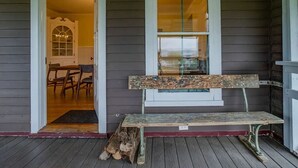 A wooden porch with a bench and a door leading to an interior room with a chandelier. - Sweet Farm on Seneca Lake (Himrod)