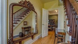 A staircase with a wooden railing, a large ornate mirror, and a dining area with chairs and a table. - Sweet Farm on Seneca Lake (Himrod)