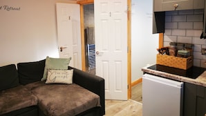 Um quarto aconchegante com sofá, cozinha compacta e porta para outro espaço.