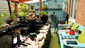 Um jardim tranquilo com lago para carpas, estátua de Buda e diversos vasos de plantas.