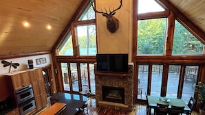 Un intérieur de cabine spacieux, agrémenté d’une cheminée en pierre, d’un plafond en bois et de grandes fenêtres.
