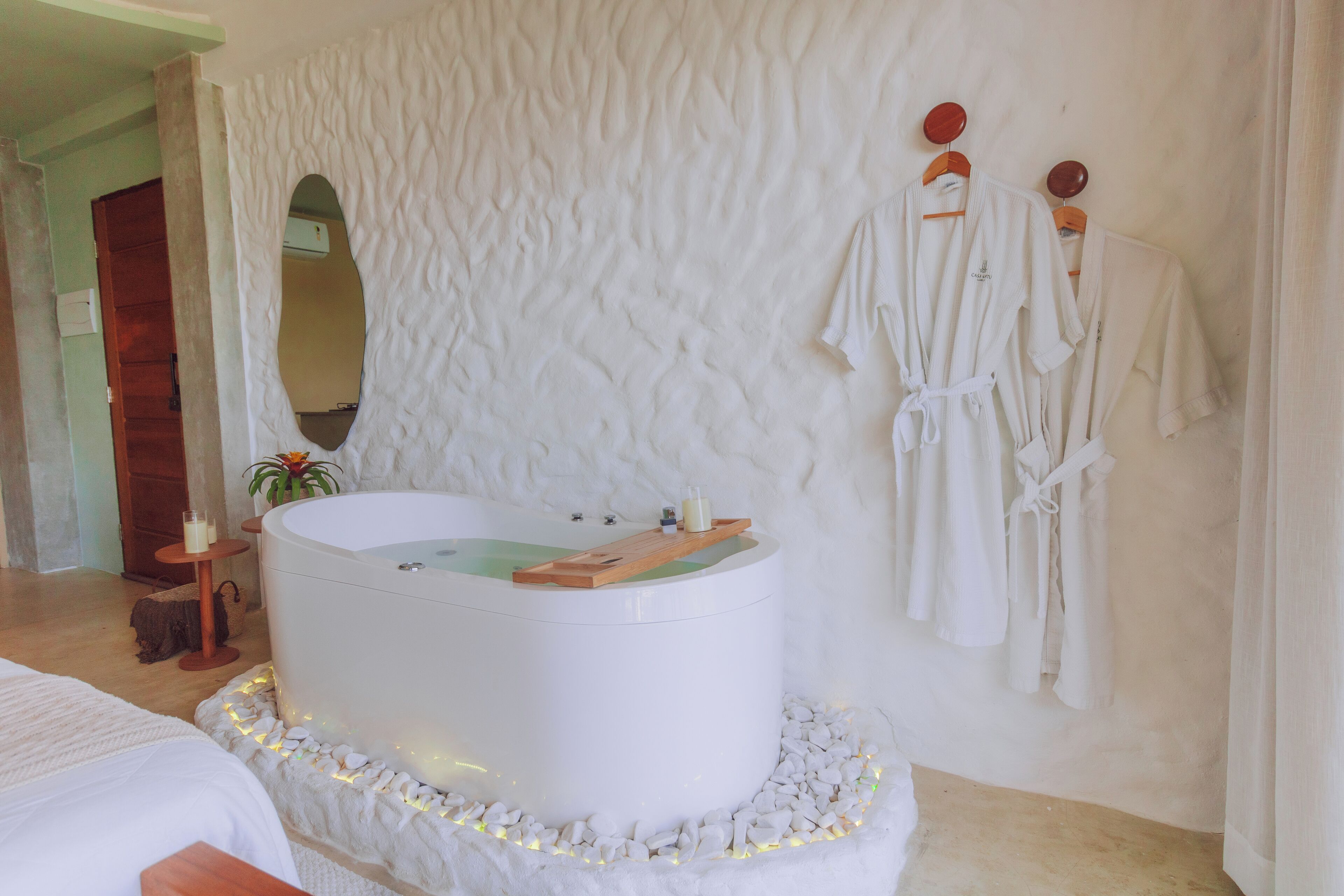 A spa room with a large bathtub, white towels, and a wooden shelf.