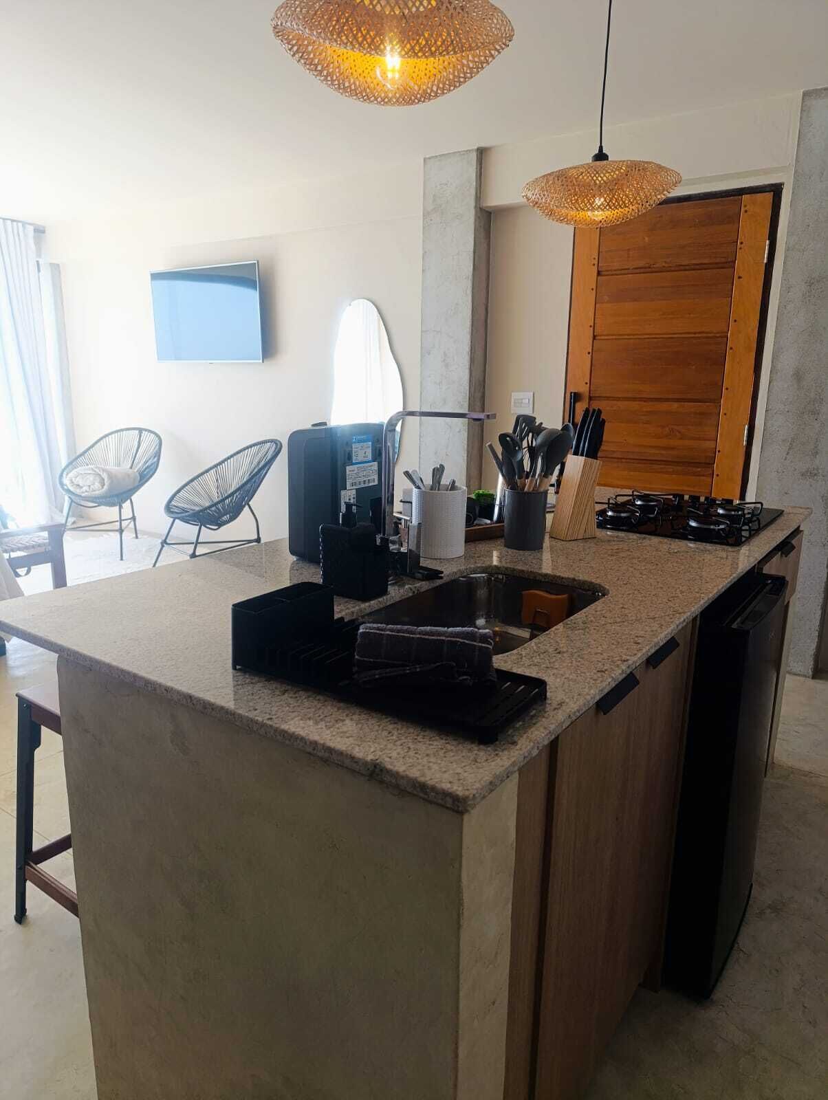 Une cuisine moderne avec un plan de travail en granit, une cuisinière encastrée et un évier. On peut voir deux chaises, une machine à café et un bloc à couteaux.
