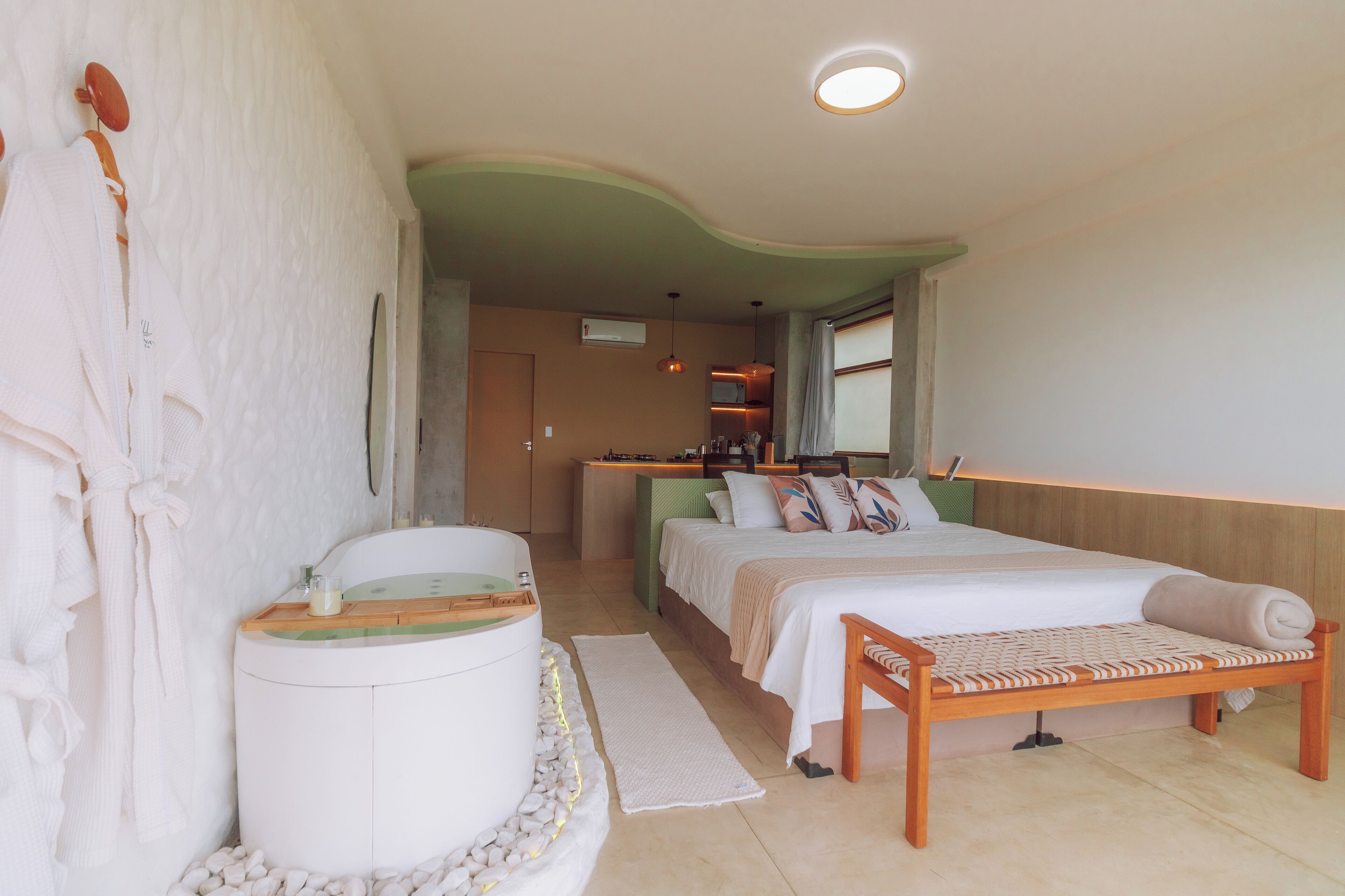 Ein Schlafzimmer mit einem Bett, einem Nachttisch, einer Bank, einer Badewanne und einem Spiegel.
