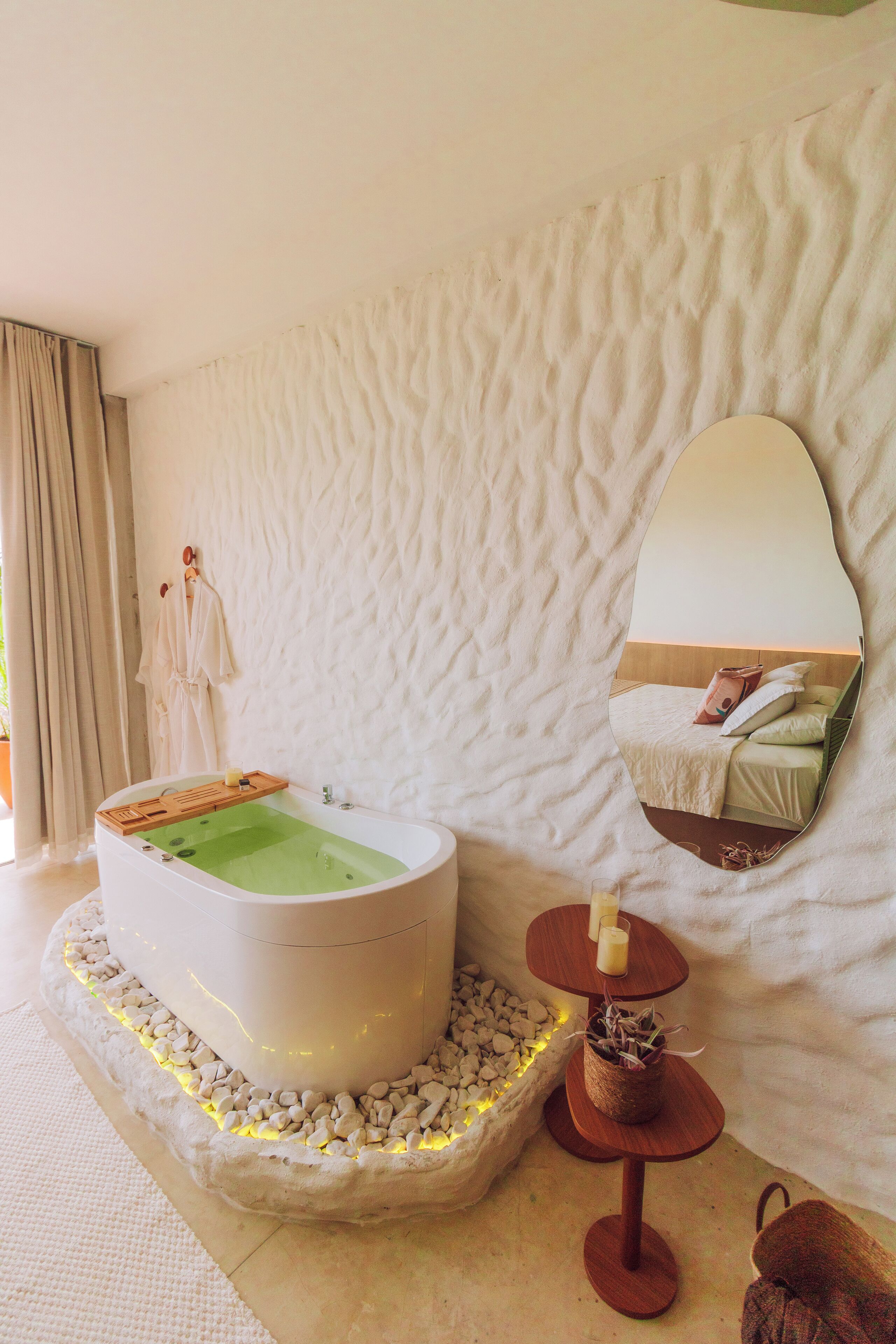A modern bathroom with a freestanding bathtub, a large mirror, and a small wooden table with candles.