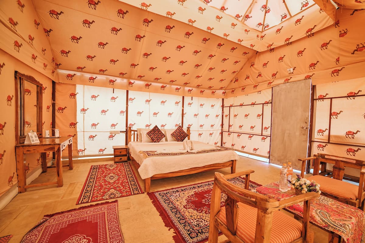 Habitación tipo tienda temática de camellos con cama, muebles de madera y alfombras estampadas.