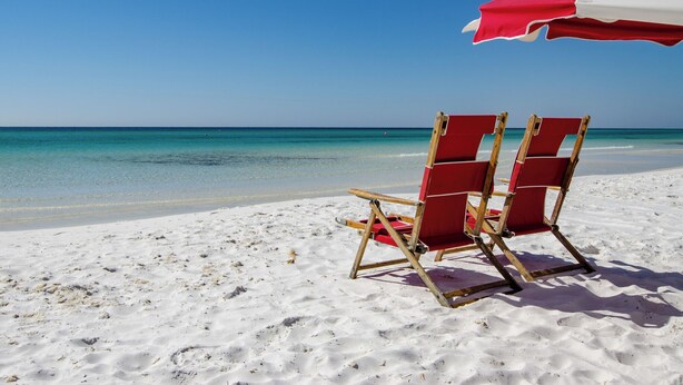 A beach scene with a red and white beach umbrella and two wooden beach chairs on the sand. - Fantastic Condo at Mediterranea (Miramar Beach)