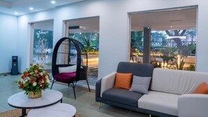 Et moderne loungeområde med en sofa, en fletstol og et bord med en blomsteropsætning.