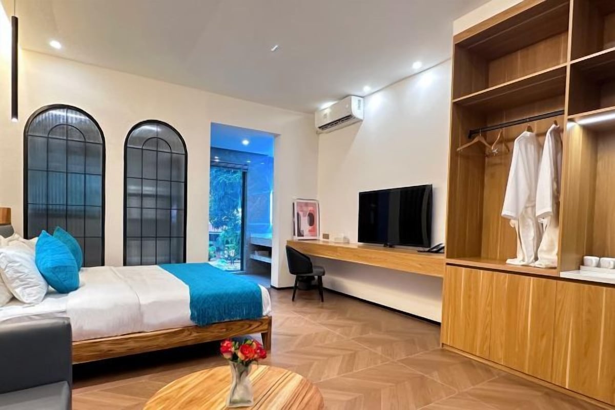 A modern hotel room with a bed, a desk, a TV, and a wardrobe.
