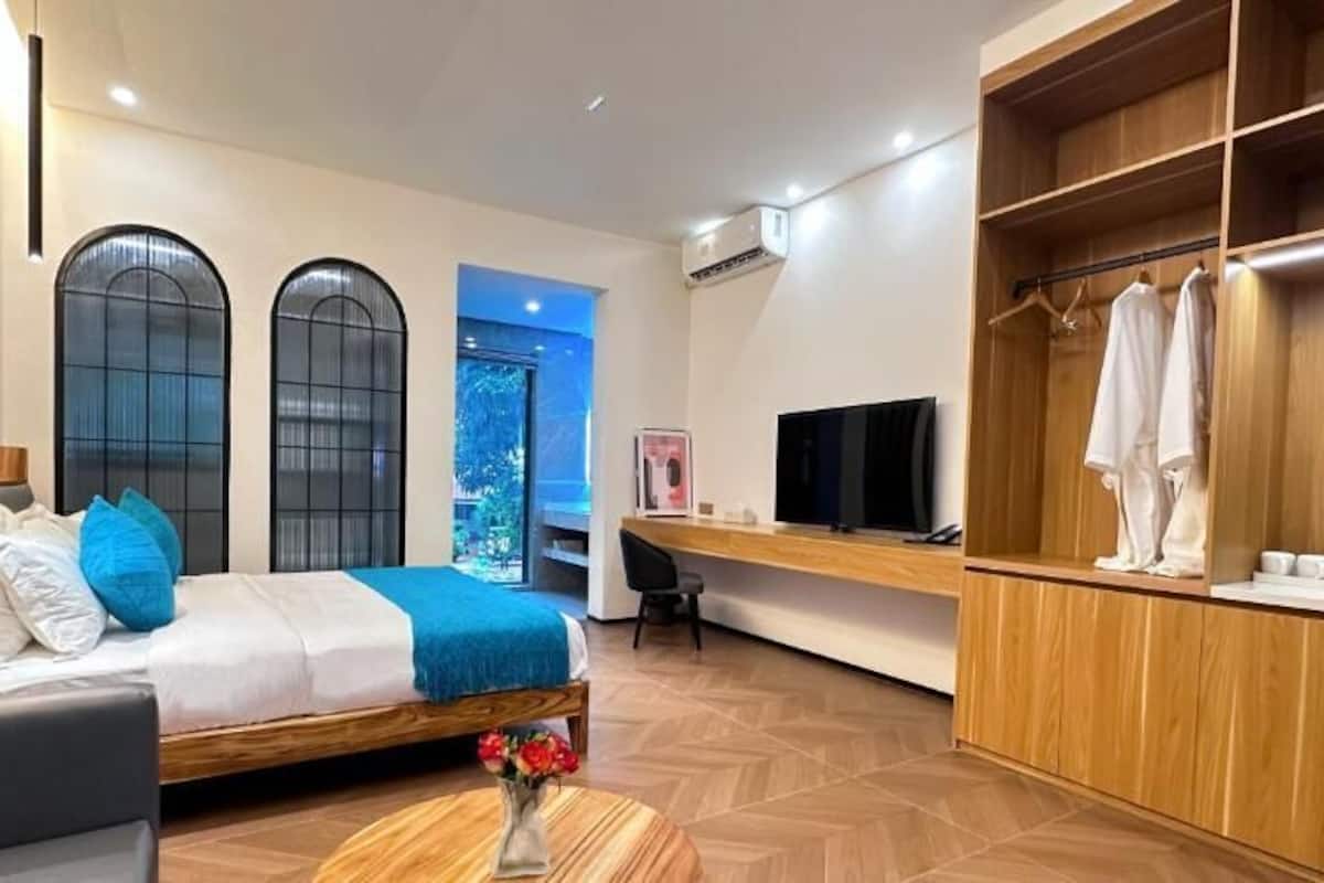 A modern hotel room with a bed, a desk, a TV, and a wardrobe.