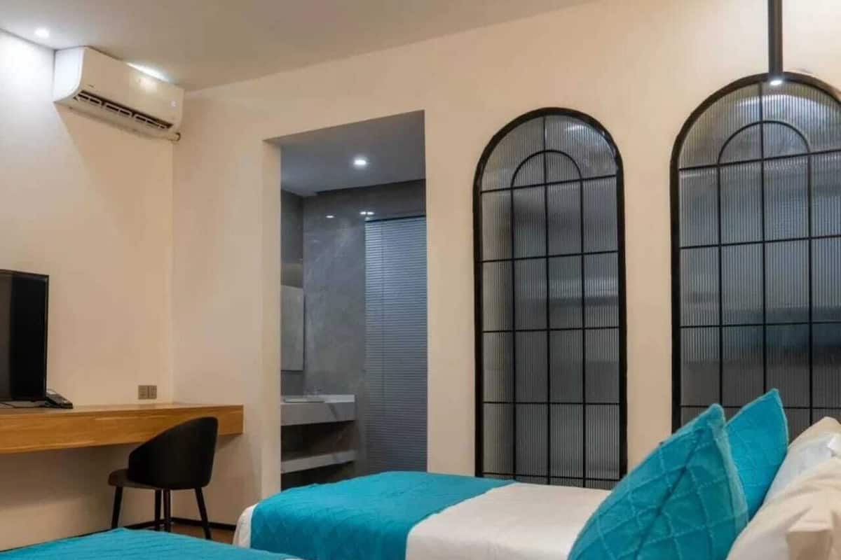 A hotel room with two beds, a desk, a chair, and a TV.