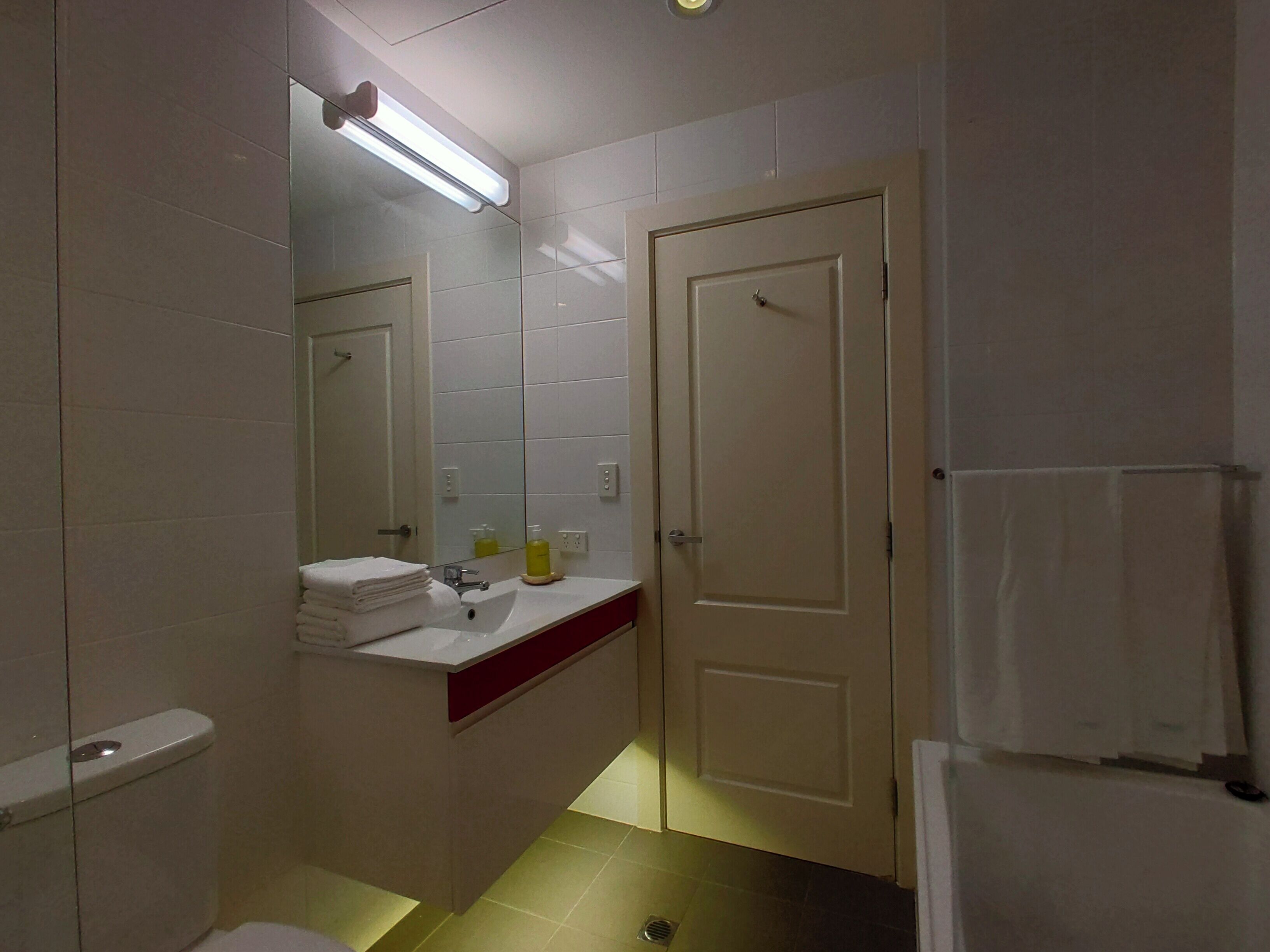 Een kleine badkamer met toilet, wastafel en spiegel. Handdoekhouder en deur zijn aanwezig.