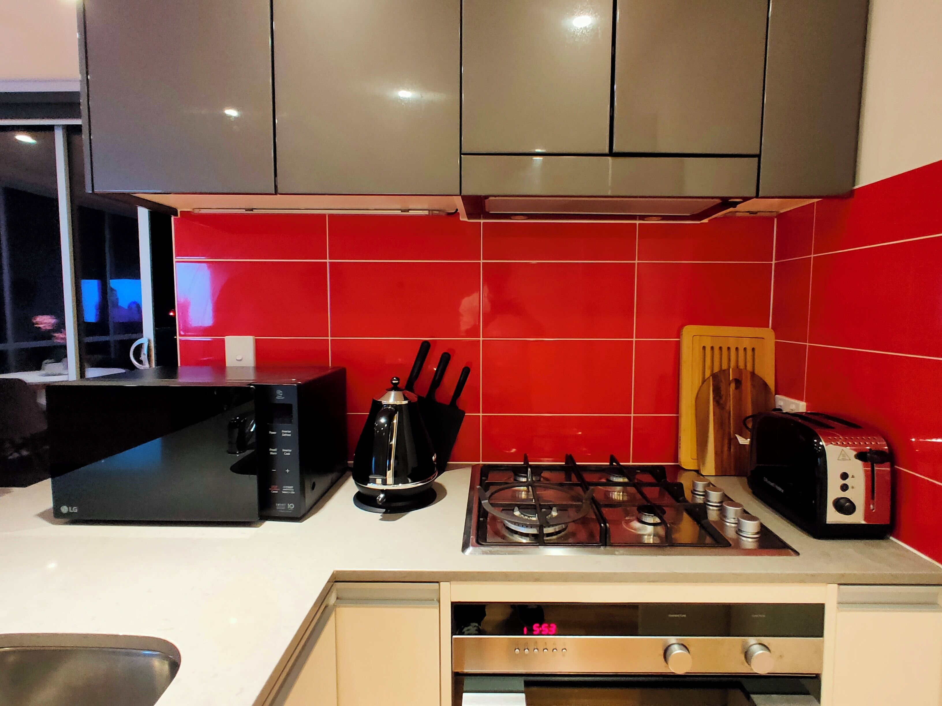 A kitchen with red tiles, a microwave, a gas stove, and a toaster.