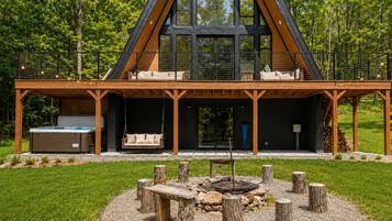 Une maison moderne dotée d’une grande terrasse, d’un jacuzzi et d’un foyer extérieur, le tout entouré de souches d’arbres.