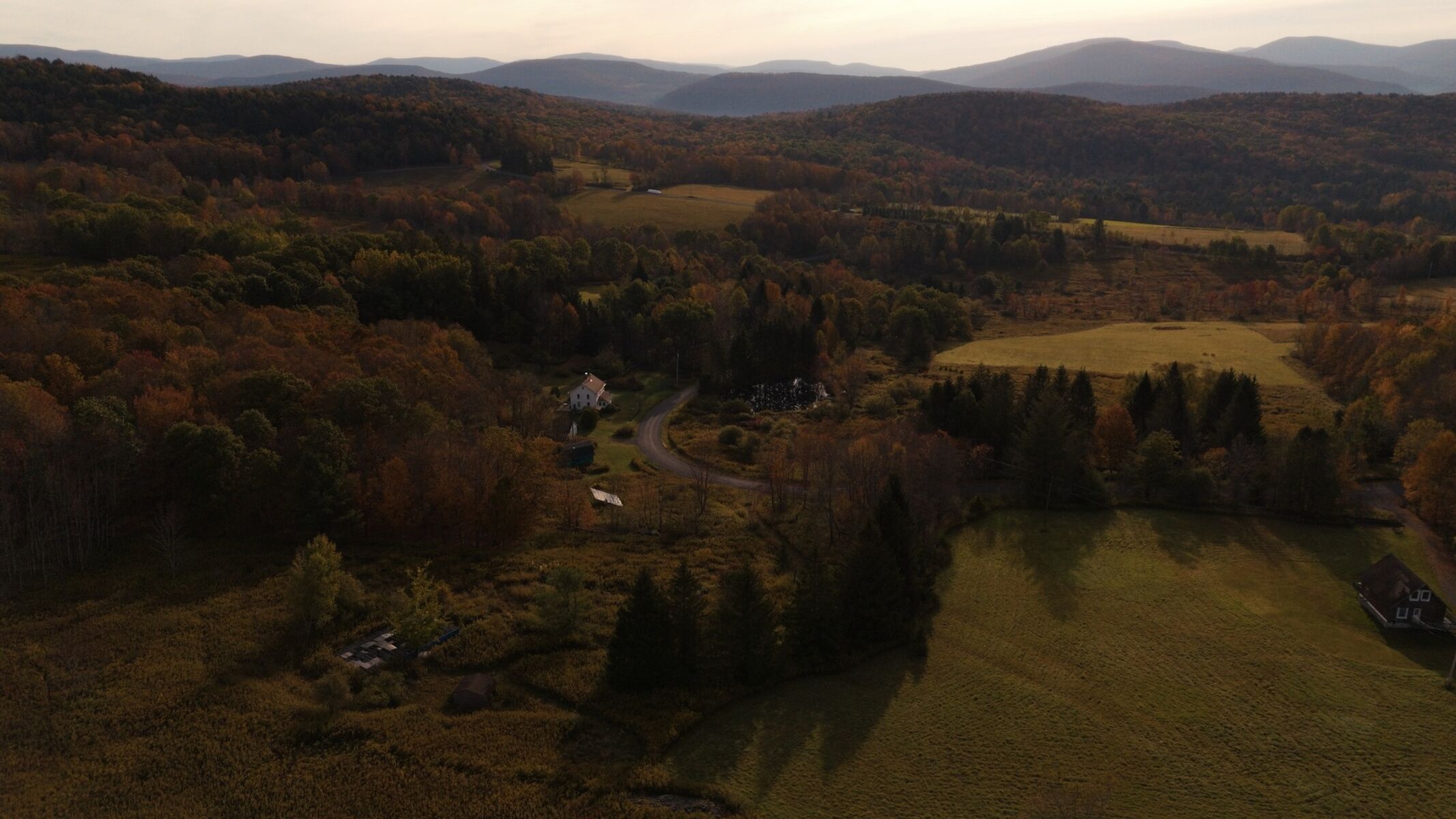 Landskab med snoet vej, et lille hus og marker i nærheden.