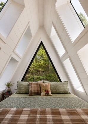 A room with a sloped ceiling and skylights, a bed with patterned bedding, and a view of greenery outside.
