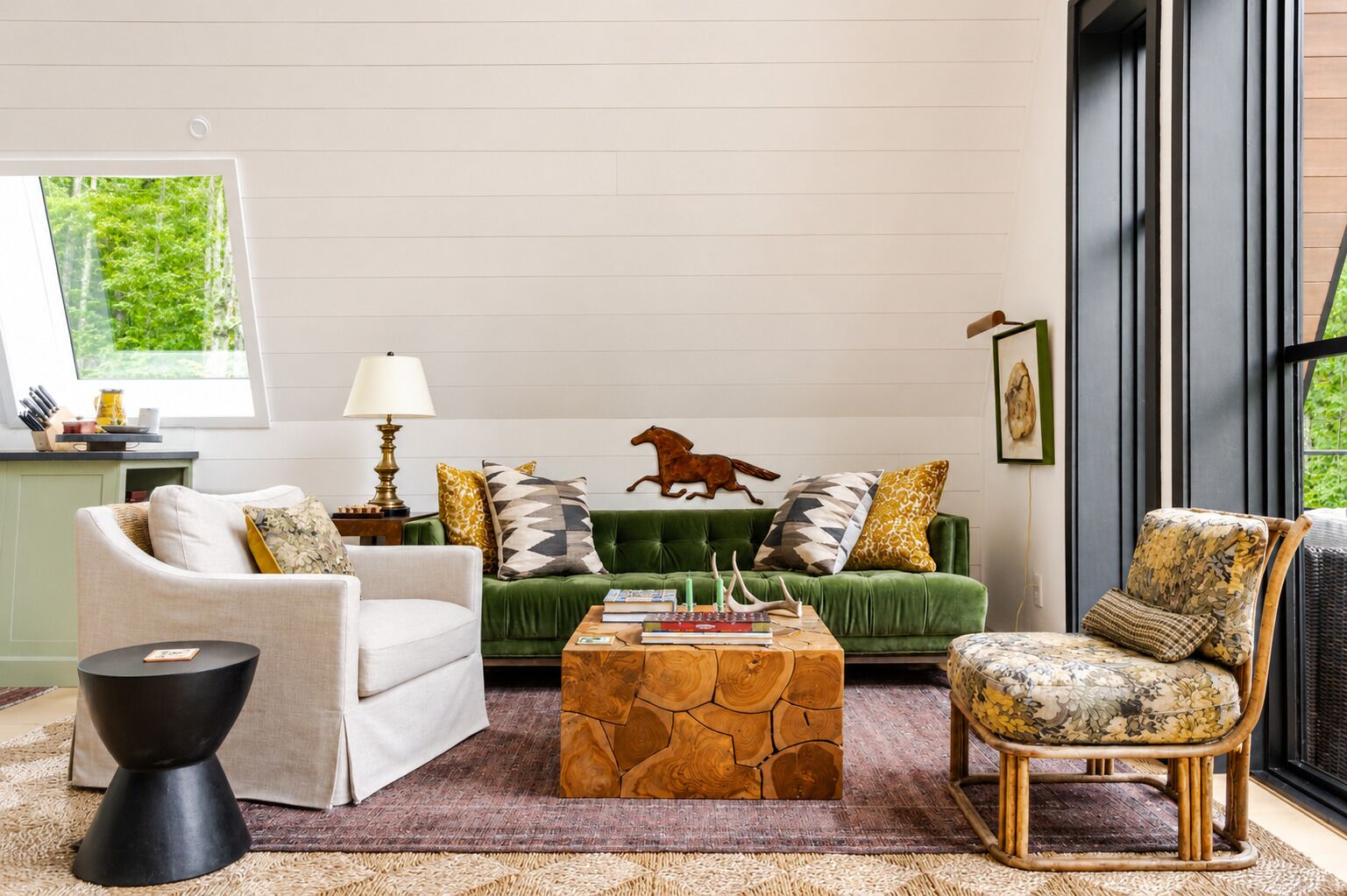 Un salon avec un canapé vert, un fauteuil blanc, une table basse en bois et un fauteuil à motifs.