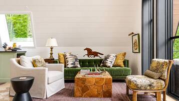 Un salon avec un canapé vert, un fauteuil blanc, une table basse en bois et un fauteuil à motifs.