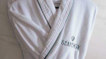 A white robe with "SEANERGY" embroidered on it, hanging on a black hanger against a marble wall.
