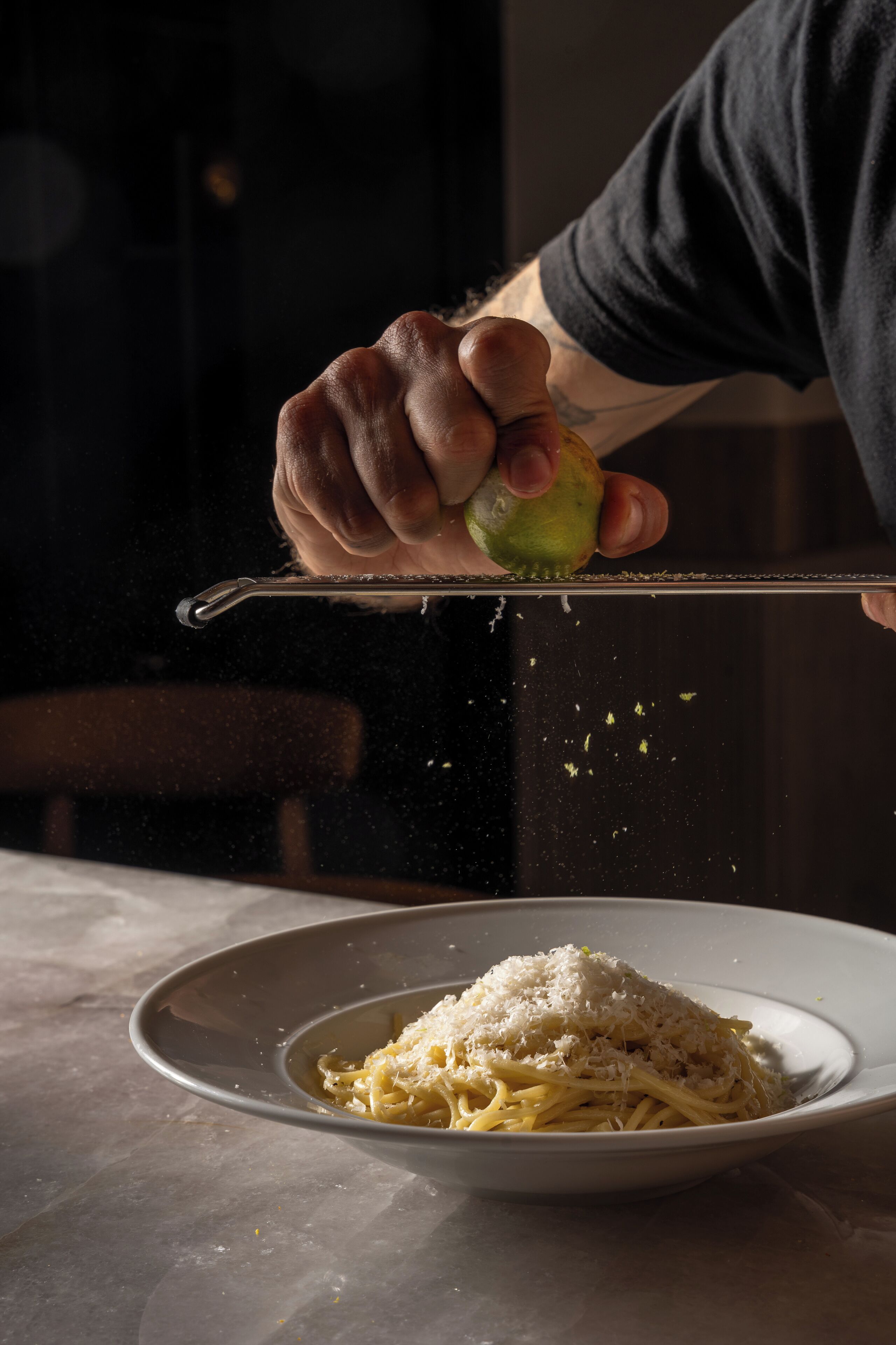 A person grating cheese over pasta.