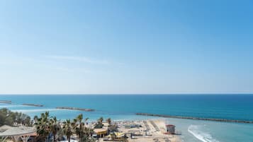 A beach resort with a sandy beach, palm trees, and a clear blue sky.