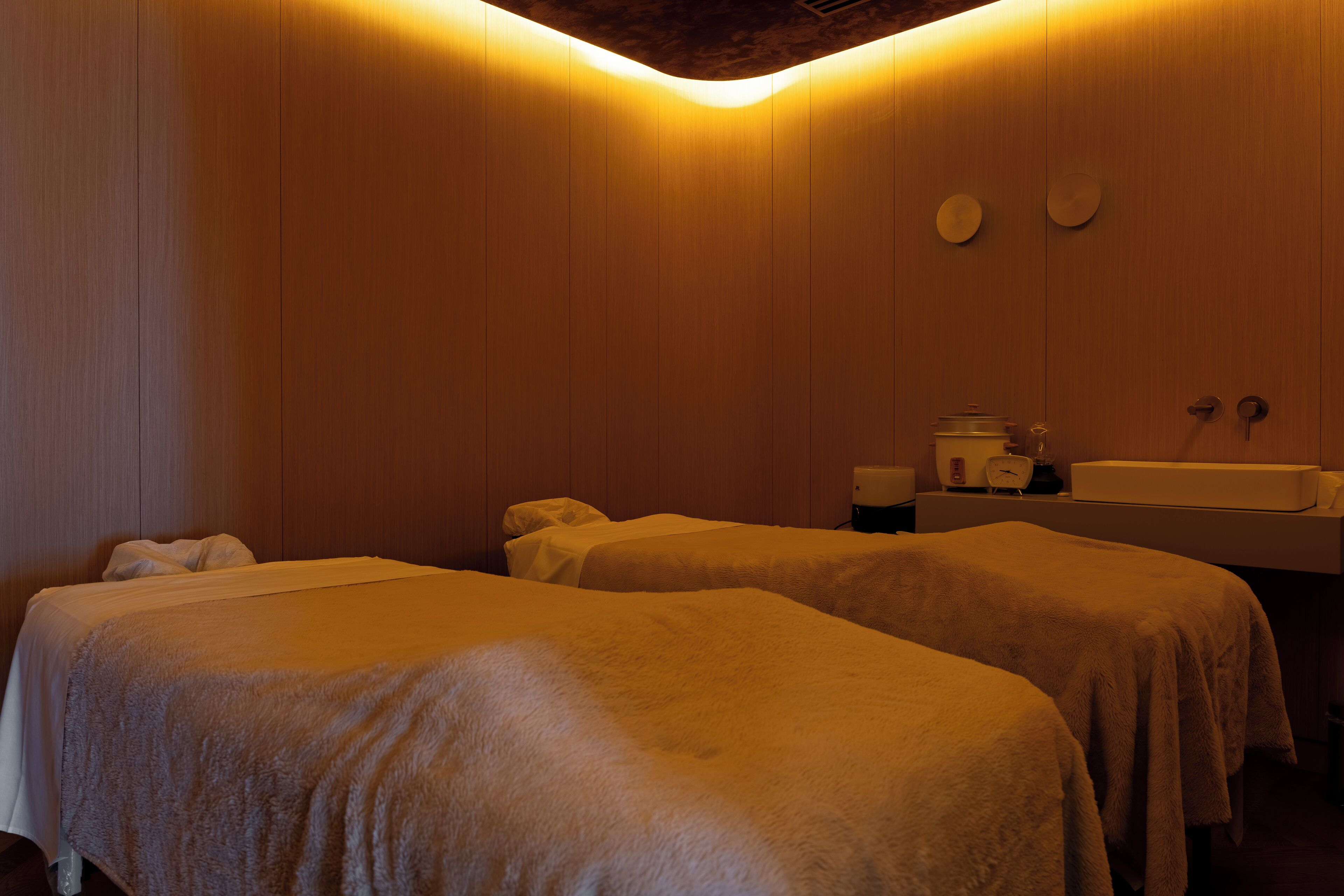 Une chambre avec deux lits recouverts de draps blancs, un mur en bois et un lavabo avec un miroir.