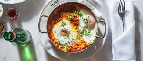 A breakfast setting with a plate of eggs, a fork, and a glass of water on a table.