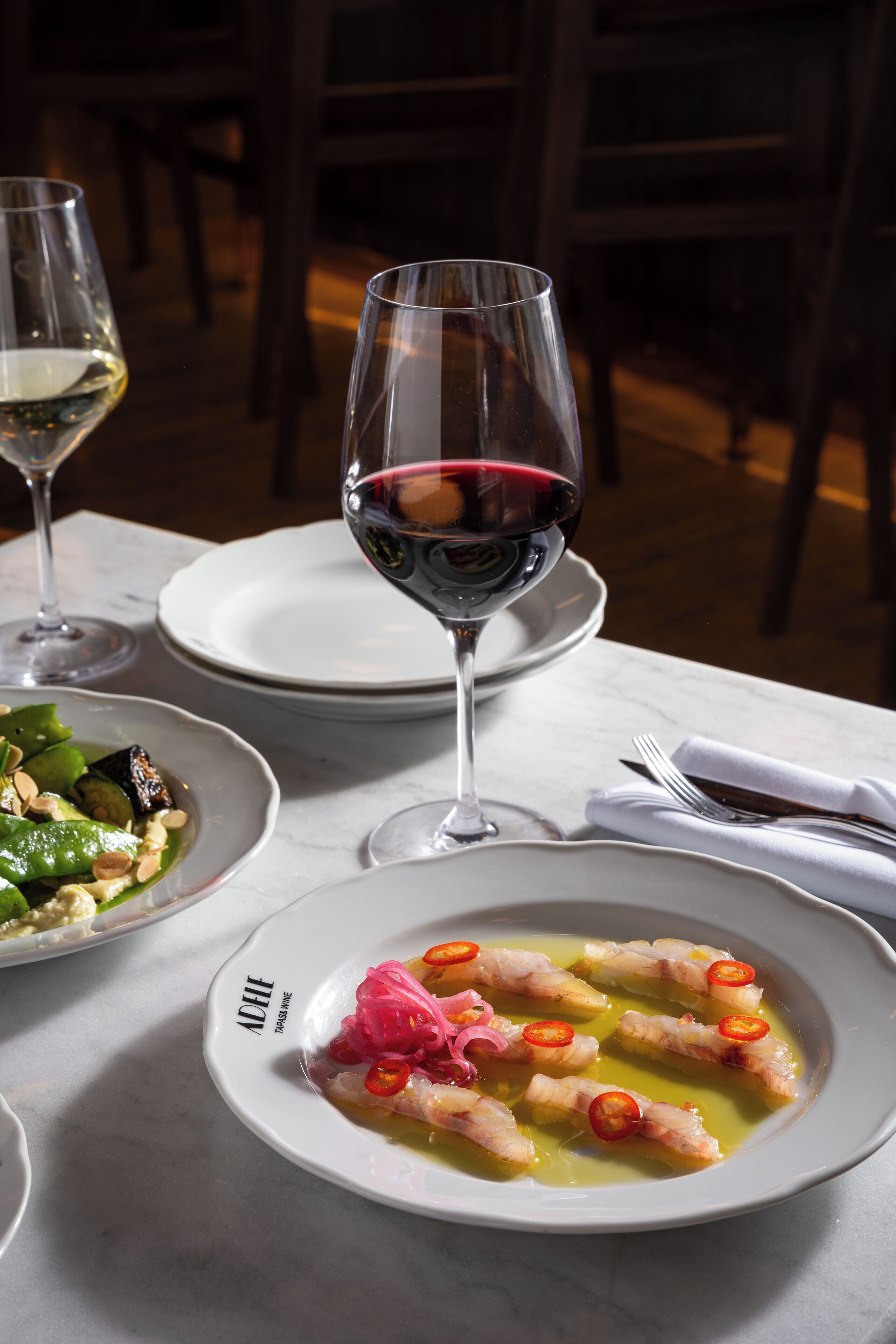 A dining table with plates of food, a glass of red wine, and a glass of white wine.