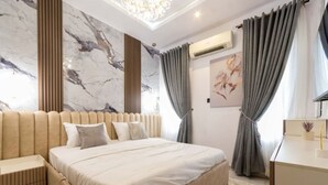 A modern bedroom with a large bed, a bedside table, a chest of drawers, and a marble-patterned wall. - Lux Lekki Home w PS5 Balcony 24 7 Power Security (Lekki)