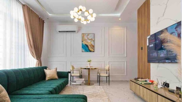 A modern living room with a green sofa, a round table, and a TV on the wall. - Lux Lekki Home w PS5 Balcony 24 7 Power Security (Lekki)