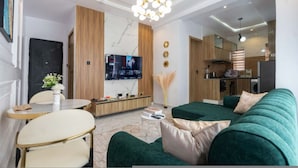 A modern living room with a green sofa, a dining table, and a TV mounted on the wall. - Lux Lekki Home w PS5 Balcony 24 7 Power Security (Lekki)