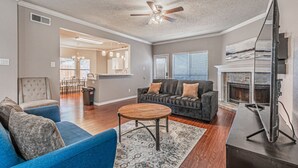 A living room with a blue sofa, a grey sofa, a wooden coffee table, and a fireplace. - Lux 3-br Garage Gated Yard by The Star Frisco (Frisco)