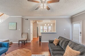 Un salon spacieux doté de planchers en bois franc, d’un canapé gris, d’un fauteuil bleu et d’un ventilateur de plafond.